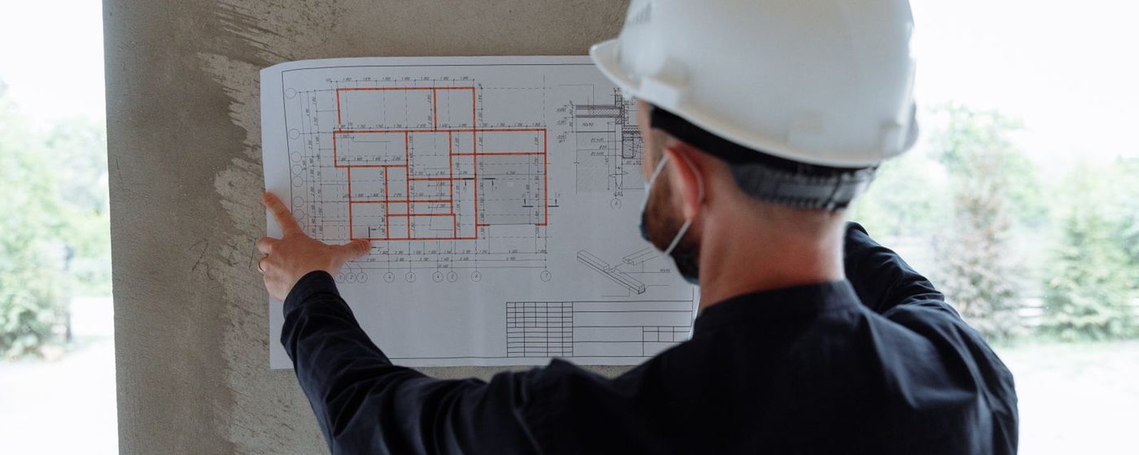 Técnico de capacete analisando planta fixada em pilar de concreto