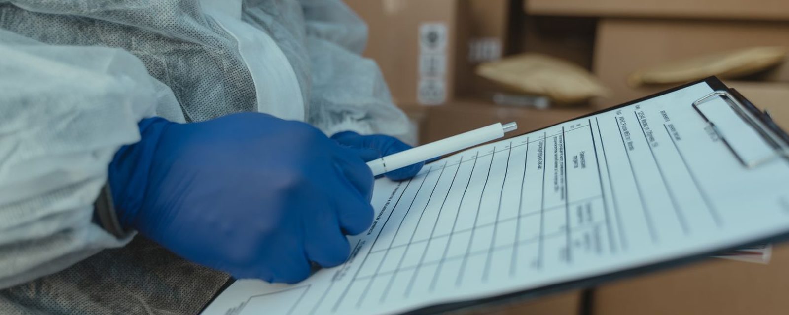Mão com luva registrando dados em formulário de prancheta