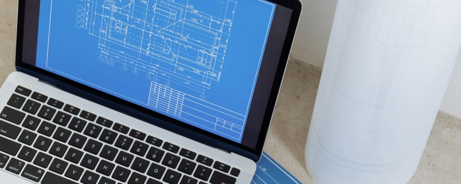 Notebook exibindo projeto técnico ao lado de pranchas enroladas